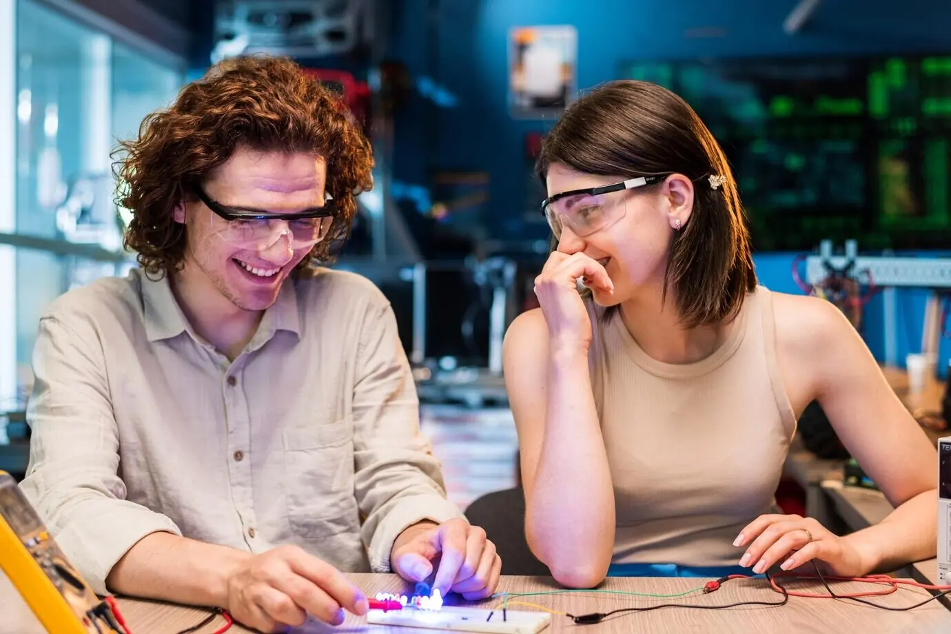 Begeisterter junger Mann und junge Frau tragen Schutzbrillen und experimentieren mit Elektrizität.